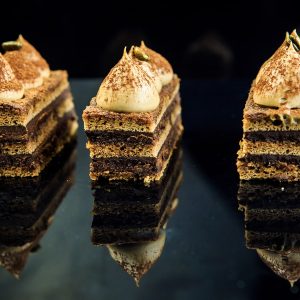 tasty chocolate opera cake slices decorated with white cream on black mirror background