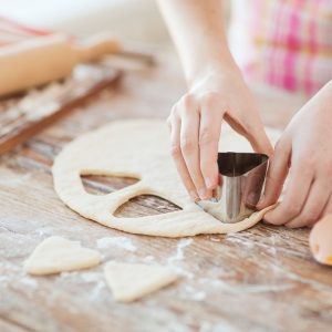 cooking and home concept - close up of female hands making cookies from fresh dough at home