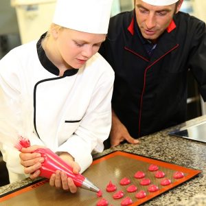 Student in pastry making cookies with help of teacher
